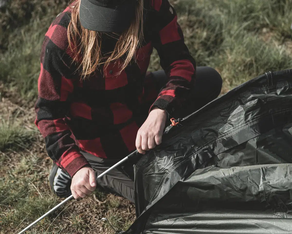 Vrouw zet de Easy Camp Sarek 1 Tent op en houdt tentstokken vast, eenvoudig en snel op te zetten.